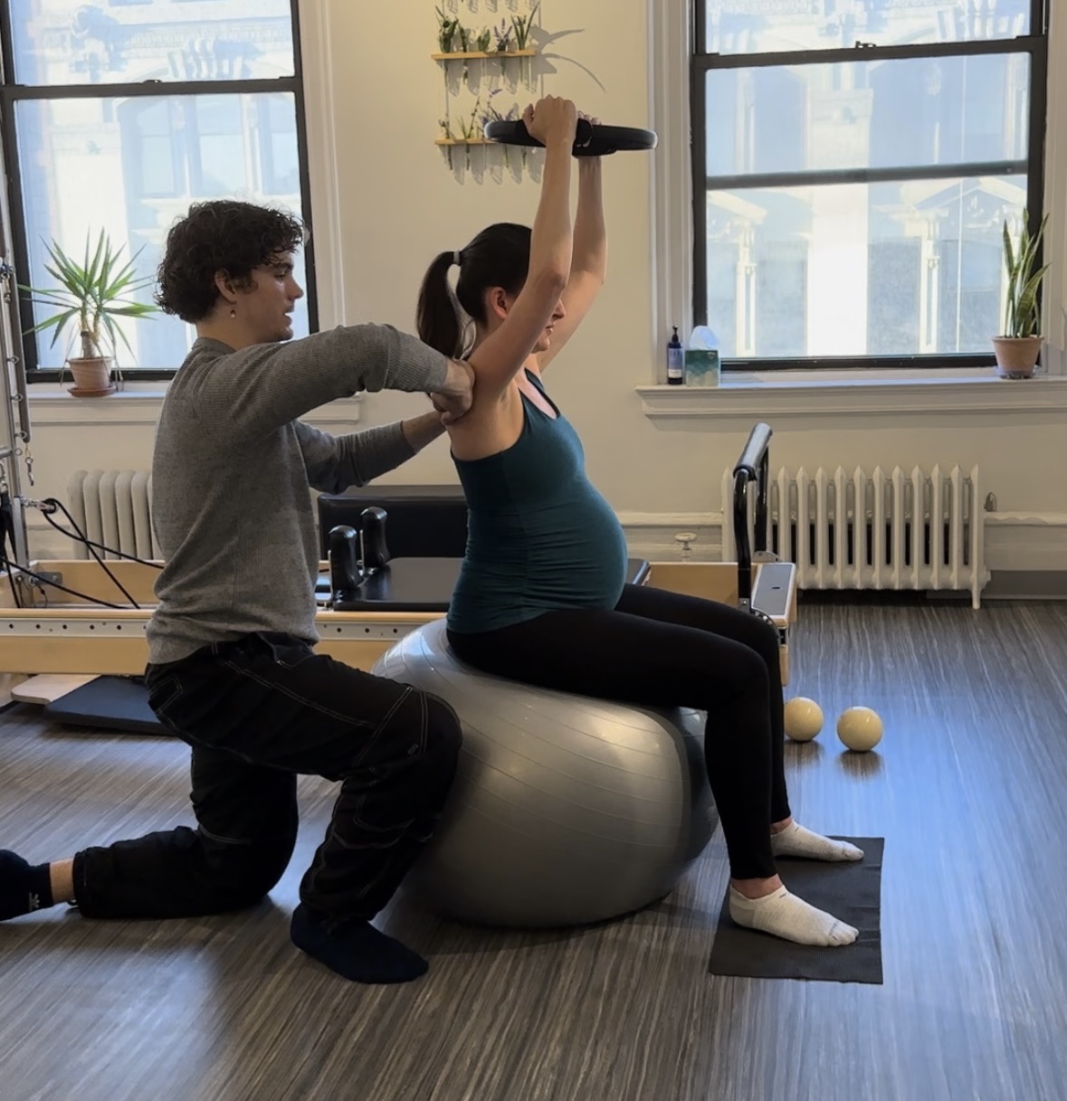 Pilates instructor teaches Pilates biomechanics to 2nd trimester pregnant woman sitting on a stability ball