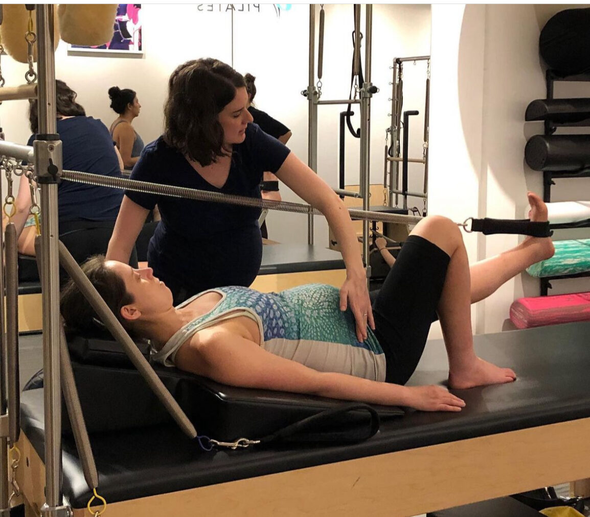 A woman in her 2nd trimester of Pregnancy does prenatal Pilates in a one-on-one session using the Pilates Cadillac