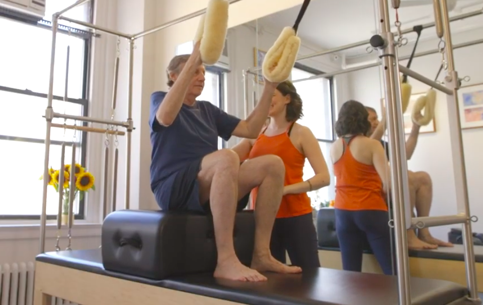 Female Pilates instructor teaches an man over 60 to build strength on the Pilates Cadillac