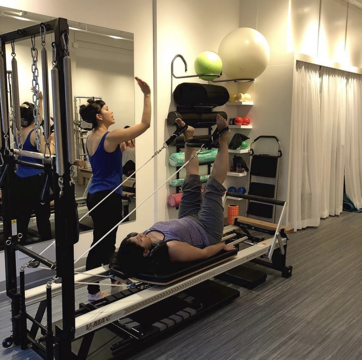 Pilates client on the reformer with legs in the straps being directed by her Pilates instructor